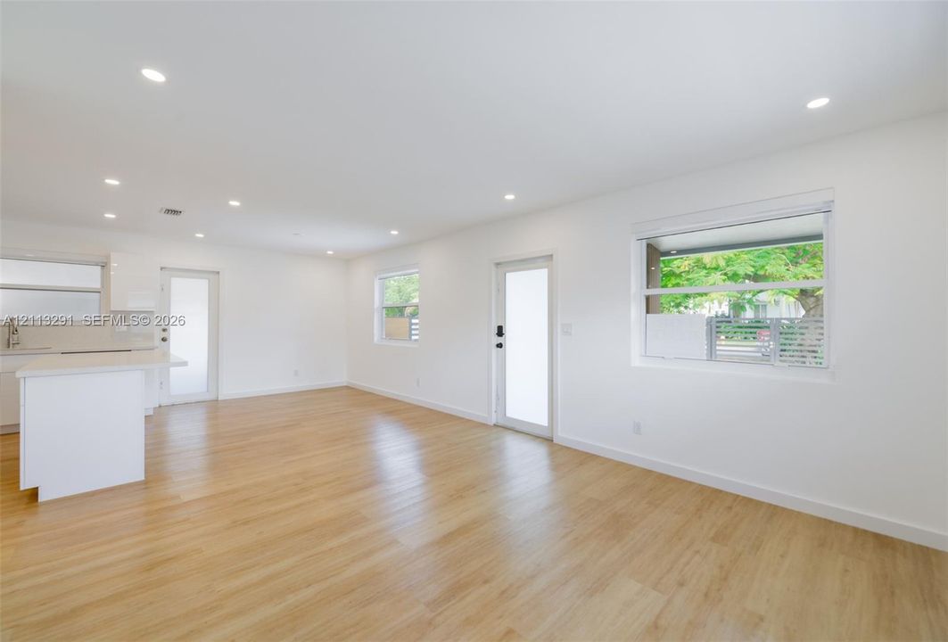 Open-concept space featuring recessed ceiling lighting, light-toned wood-finish flooring, white walls, and multiple windows with white frames