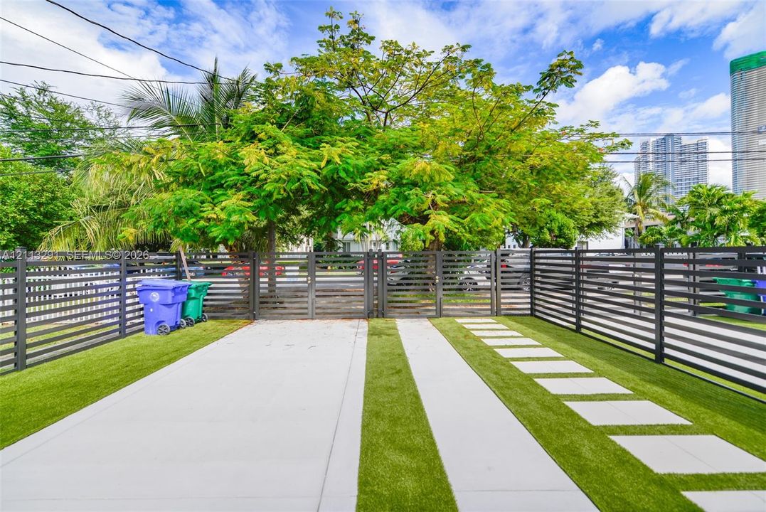 Enclosed outdoor space featuring a concrete parking pad, horizontal slat privacy fencing, synthetic turf, and square concrete pavers