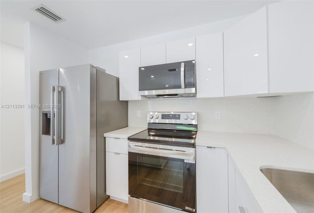 Kitchen featuring white high-gloss cabinetry, stone-finish countertops, stainless steel appliances, and wood-finish flooring