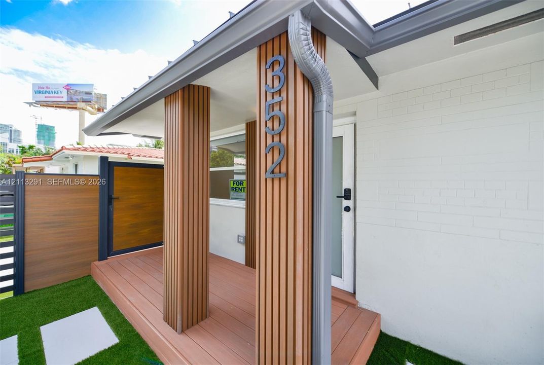 Entrance featuring a composite deck, vertical wood-slat accent columns, white painted brick exterior, and a privacy fence with a matching wood-finish gate