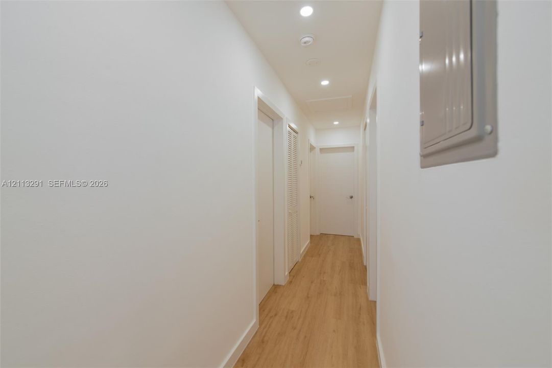 Hallway featuring wood-finish flooring, recessed lighting, and multiple interior doors with louvered closet detailing