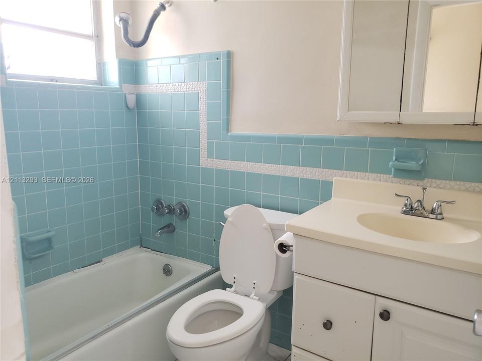 Bathroom featuring light blue wall tile with decorative accent trim, a built-in tub with chrome fixtures, a vanity with a solid-surface countertop and integrated sink, and a wall-mounted medicine cabinet