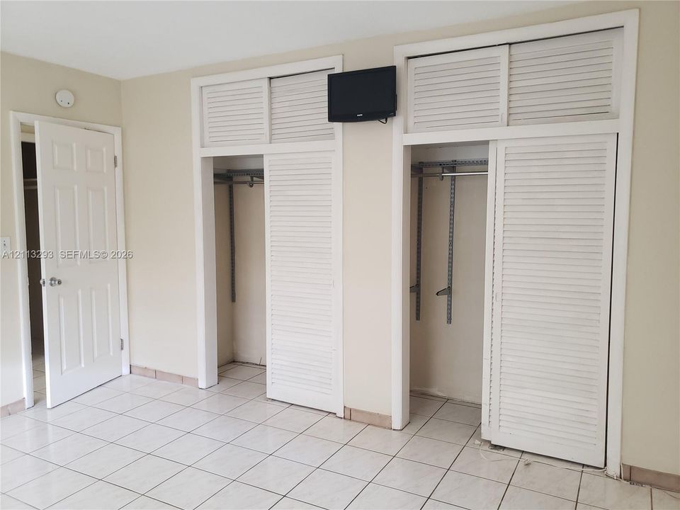 Ceramic tile flooring throughout and two dual-closet units featuring white louvered sliding doors and overhead storage compartments