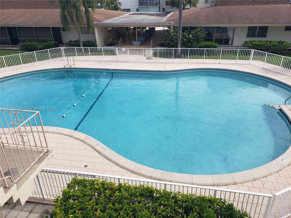 In-ground swimming pool featuring a curved concrete perimeter, tiled decking, and a white metal safety fence