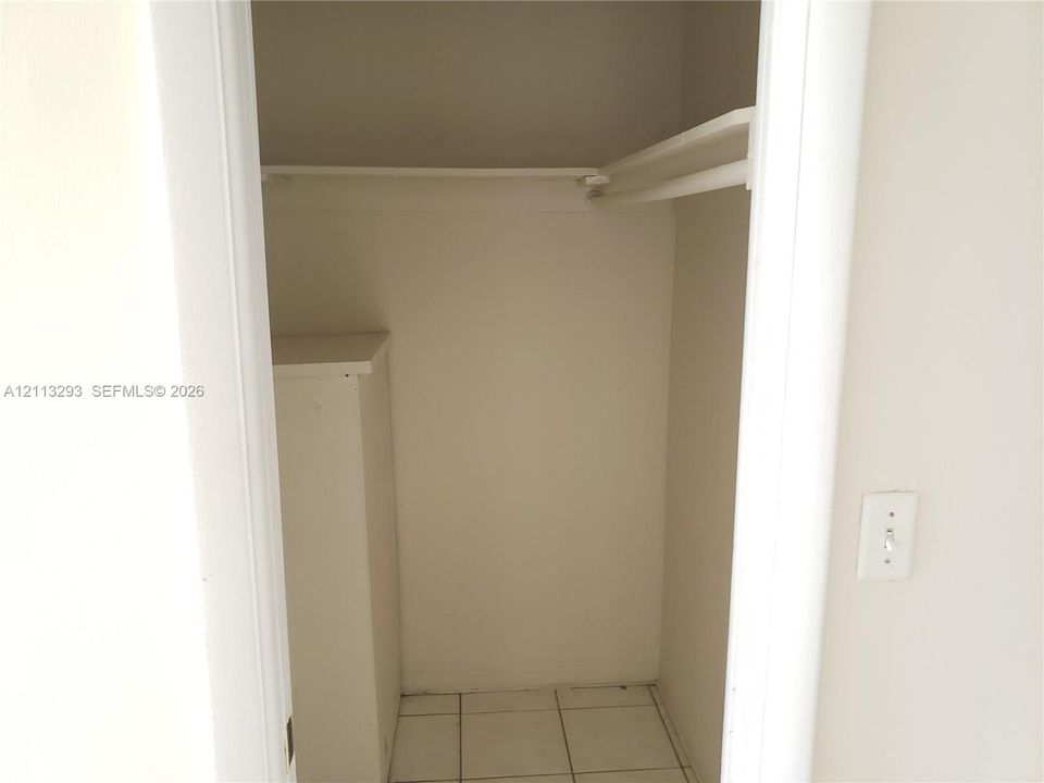 Storage closet featuring tile flooring, a built-in cabinet, and a structural hanging rod with upper shelf