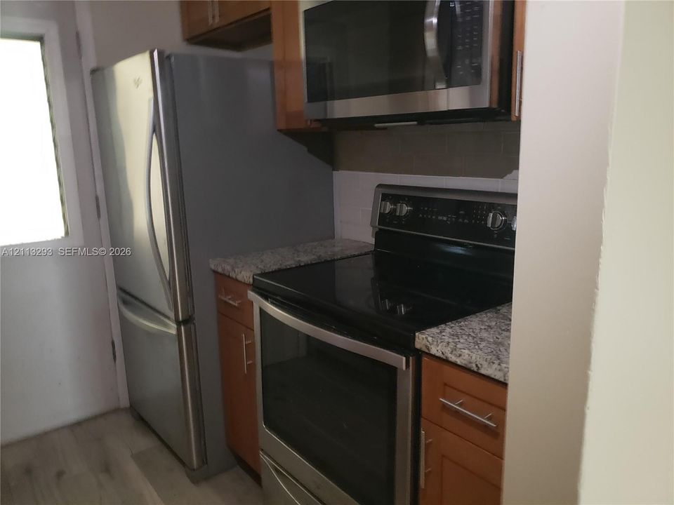 Kitchen featuring stainless steel appliances, stone-patterned countertops, wood-finish cabinetry, and a neutral tile backsplash