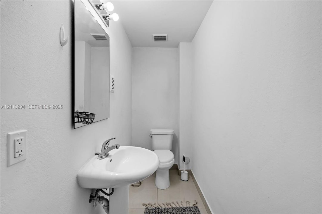 Wall-mounted mirror with integrated lighting, pedestal sink with metal faucet, and floor-mounted toilet