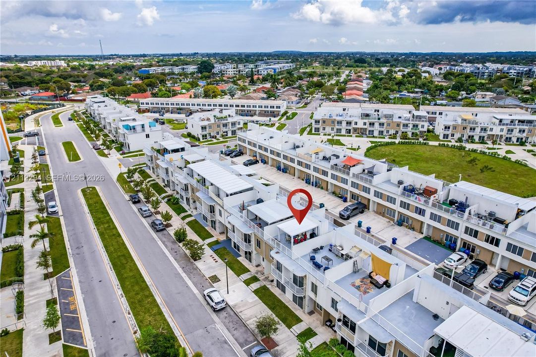 Aerial perspective of a multi-level residential structure featuring a private rooftop terrace, balcony spaces, and paved driveway parking