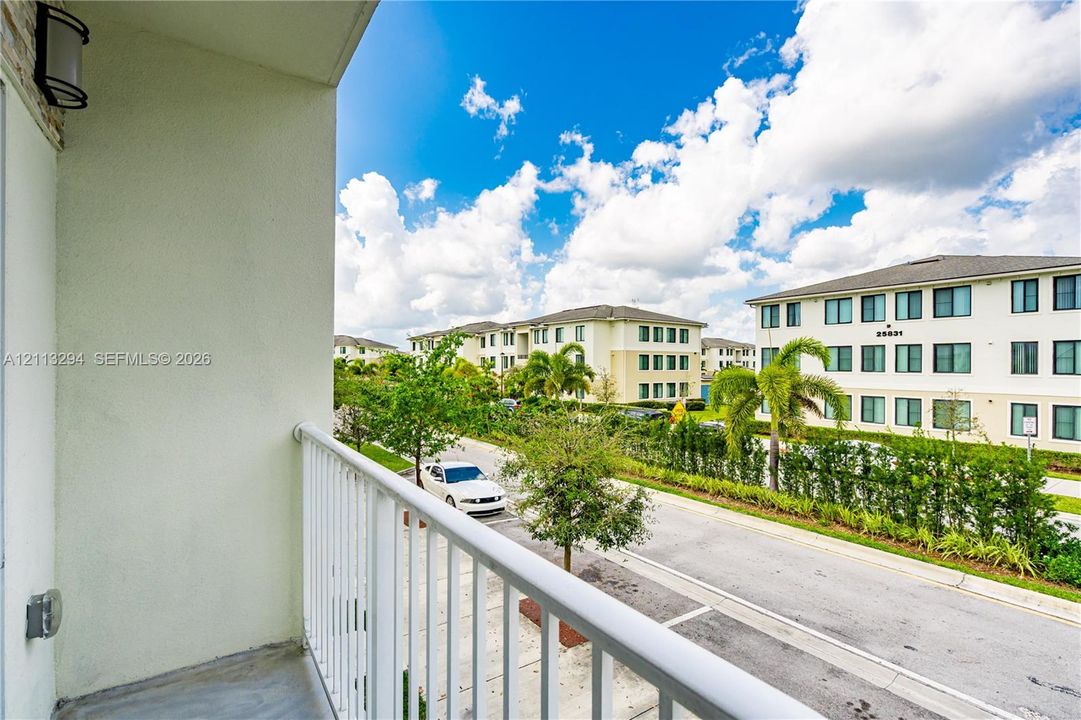 Covered balcony featuring concrete flooring, white metal railing, and wall-mounted exterior lighting