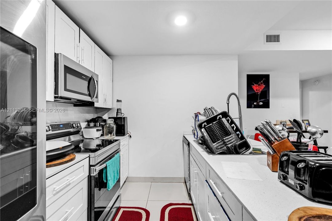 Kitchen featuring white shaker-style cabinetry, stainless steel appliances, a high-arc pull-down faucet, and light-toned countertop surfaces