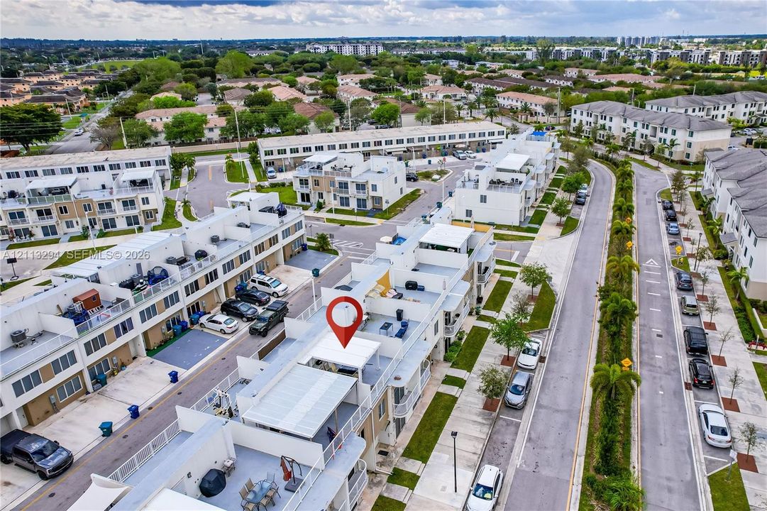 Aerial perspective of multi-level townhome featuring a rooftop terrace, metal railings, and paved surface parking