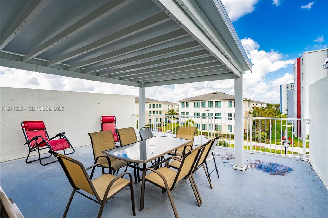 Covered balcony featuring a white metal pergola, solid stucco side walls, and white metal railing