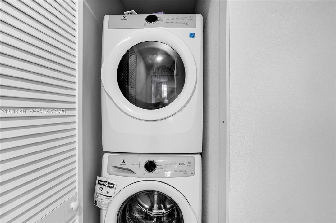 Stackable white front-load washer and dryer unit enclosed within a louvered-door closet