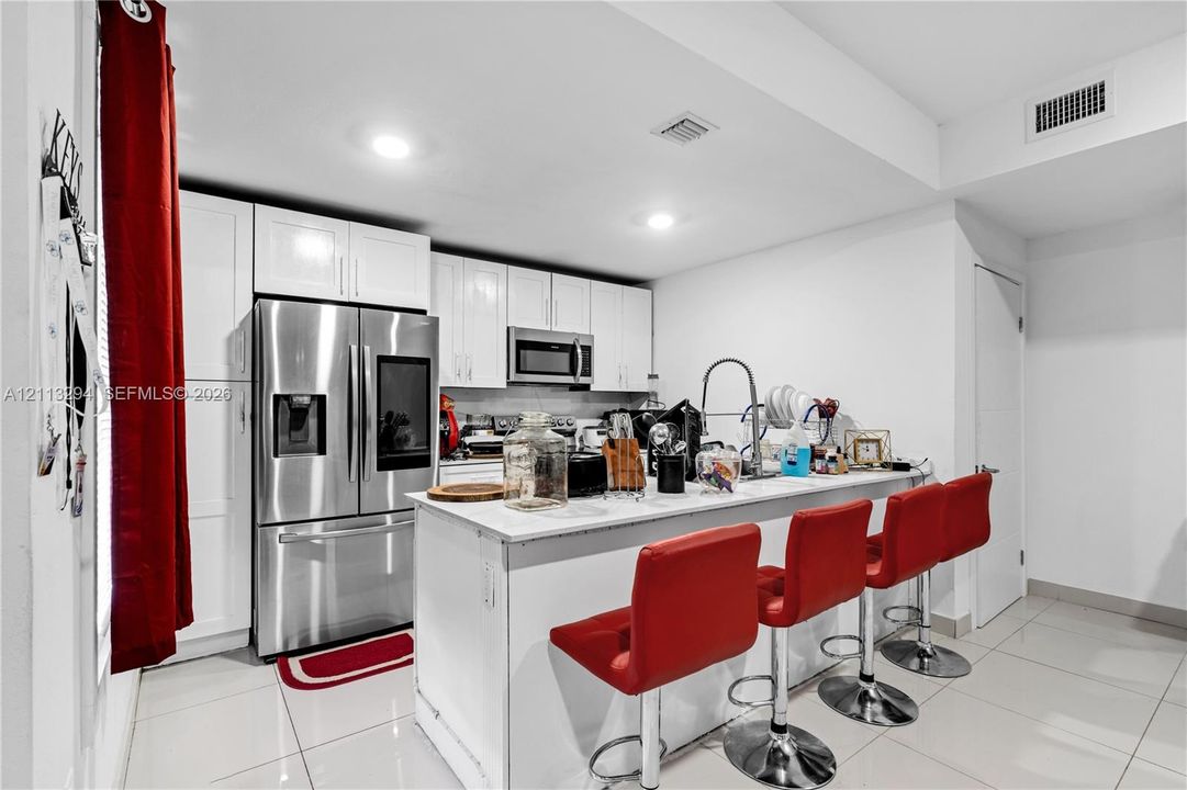 Kitchen featuring white shaker-style cabinetry, stainless steel appliances, a breakfast bar with stone-finish countertops, and large-format tile flooring