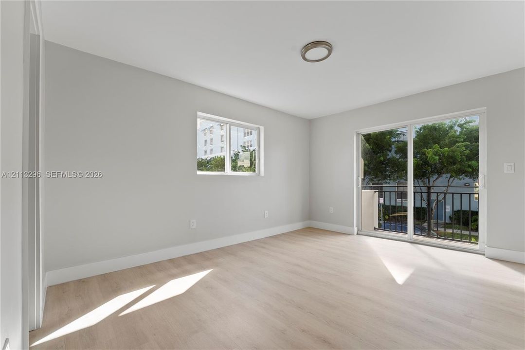 Neutral-toned interior featuring wood-finish flooring, a flush-mount light fixture, and sliding glass doors opening to a balcony with metal railing