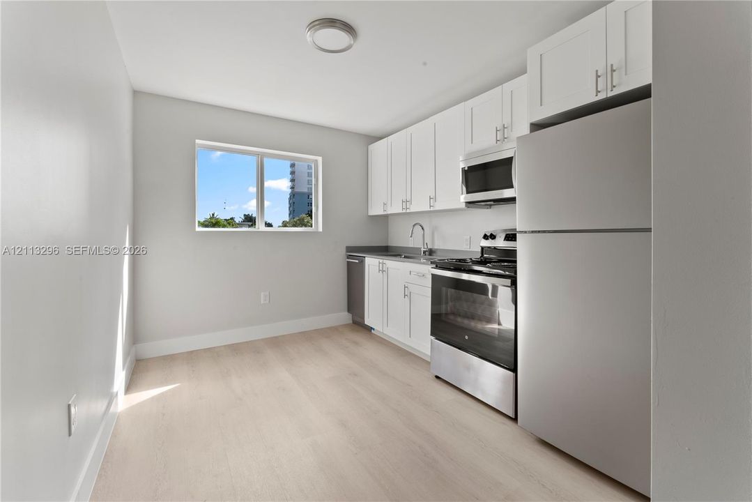 Kitchen featuring white shaker-style cabinetry, stainless steel appliances, a single-basin sink, and wood-finish flooring