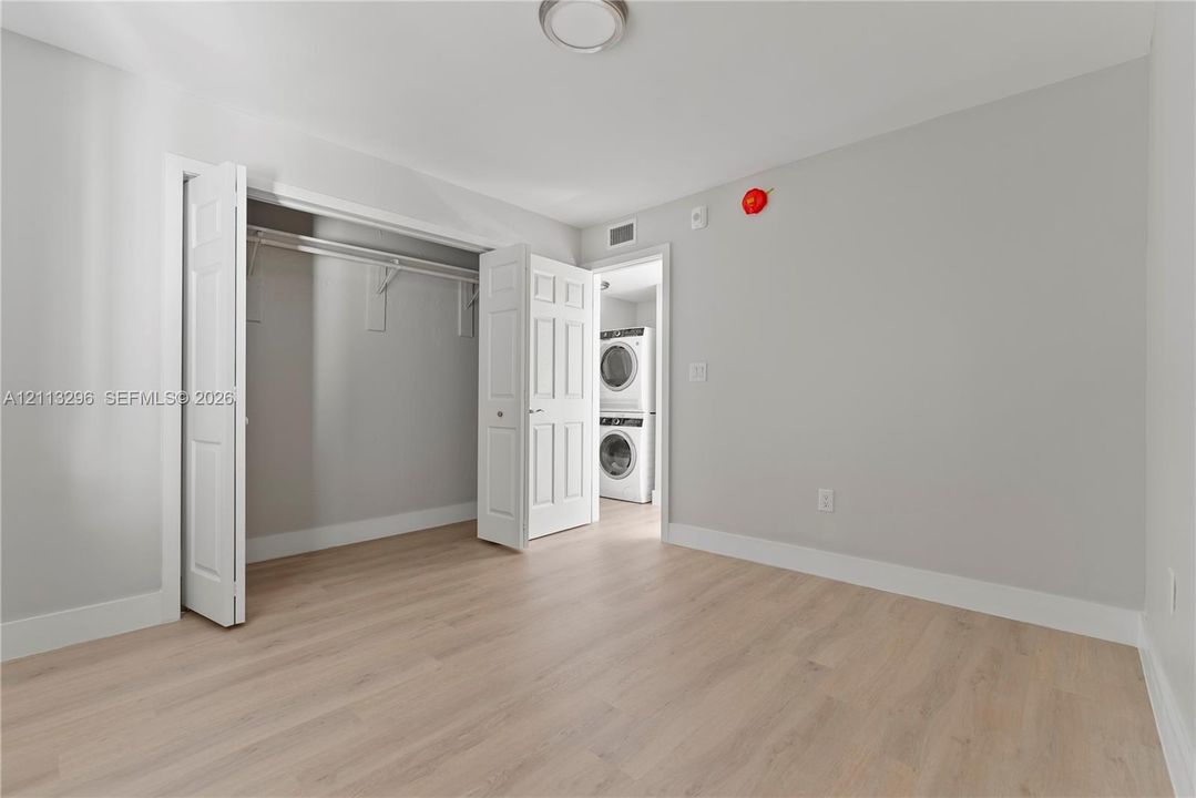 Wood-finish flooring, neutral wall tones, bi-fold closet doors, and a stacked washer and dryer unit