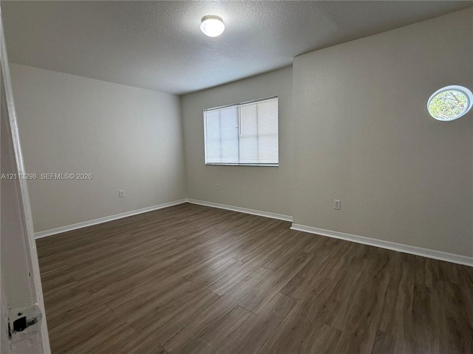Interior room featuring wood-finish flooring, a rectangular window with integrated blinds, a circular accent window, and a ceiling-mounted light fixture