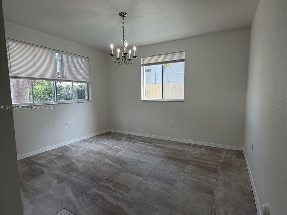 Neutral-toned tile flooring, multi-light candle-style chandelier, and large windows with horizontal blinds