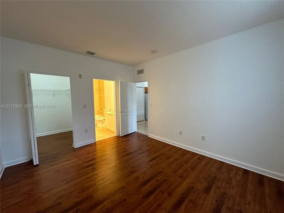 Room featuring wood-finish flooring, white walls, and built-in closet shelving