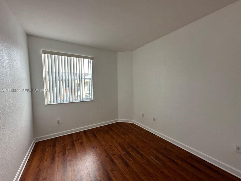 Room featuring wood-finish flooring, white walls, and a window with vertical blinds