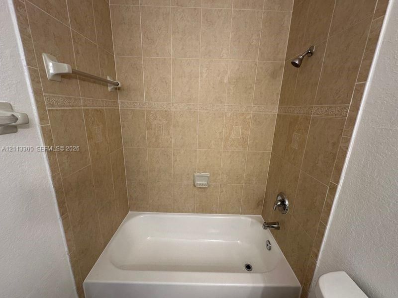 Bathtub surround featuring floor-to-ceiling neutral ceramic tiling, decorative accent border, built-in soap dish, and metal fixtures