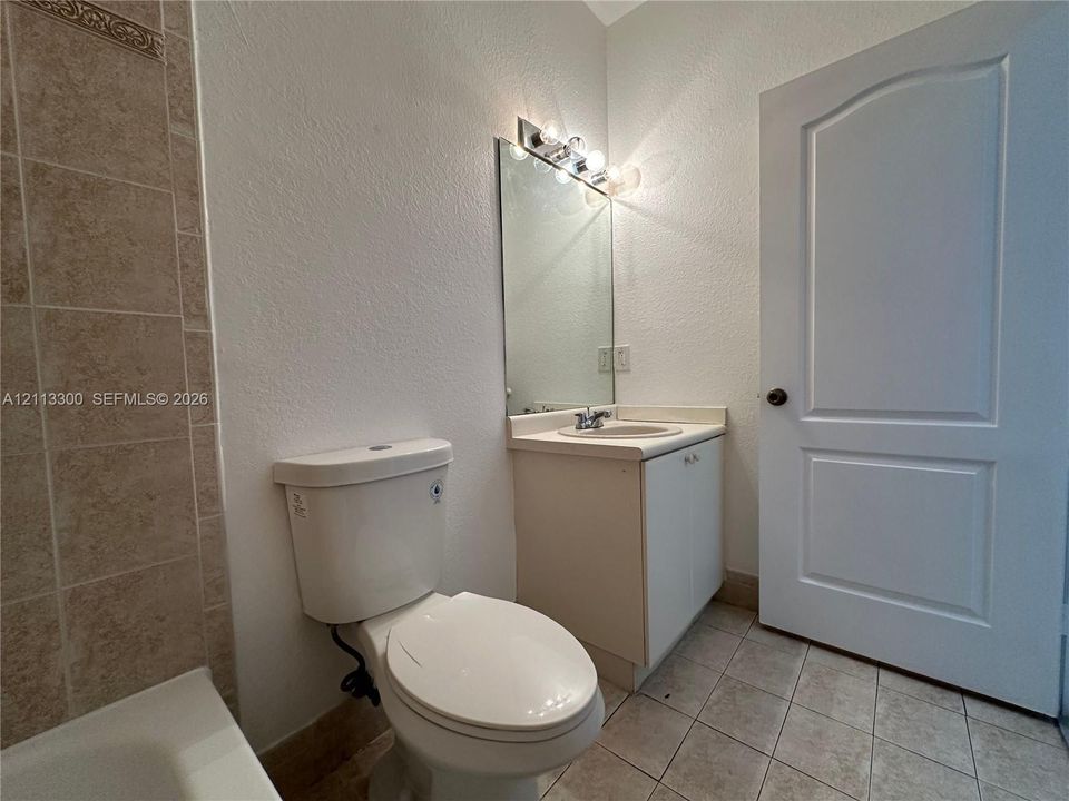 Bathroom featuring a neutral vanity with an integrated basin, tile-surround tub, wall-mounted vanity mirror, and ceramic tile flooring