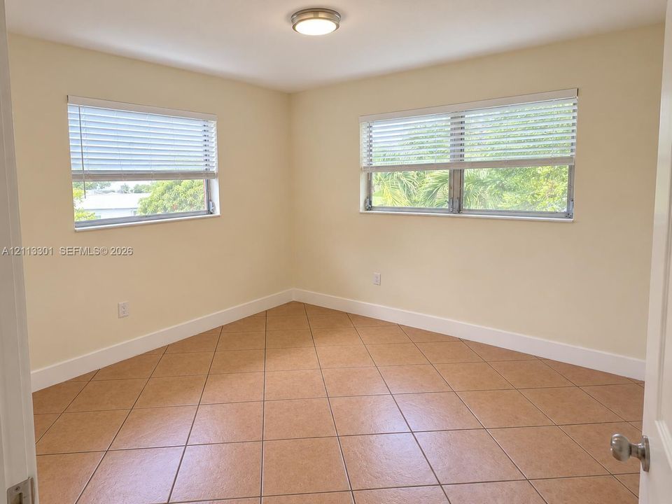 Neutral-toned interior featuring ceramic tile flooring, two horizontal windows with fitted blinds, and a flush-mount ceiling light fixture