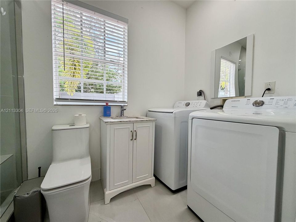 Bathroom featuring a floor-mounted toilet, vanity with a stone-finish countertop and integrated sink, wall-mounted mirror, and tile flooring