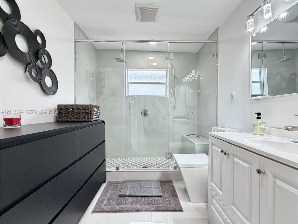 Walk-in shower with a glass enclosure, rainfall showerhead, and hexagonal tile flooring, paired with a white vanity featuring an integrated sink and chrome hardware