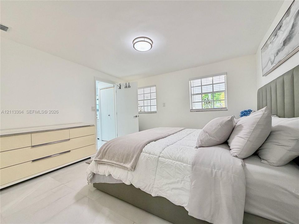 Neutral-toned interior featuring large-format tile flooring, dual-pane windows with horizontal blinds, and a circular flush-mount ceiling light fixture