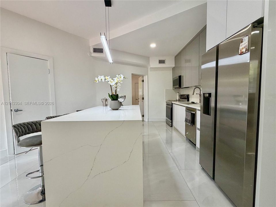 Kitchen featuring a waterfall-edge island with stone-finish countertop, high-gloss flat-panel cabinetry, stainless steel appliances, and large-format tile flooring