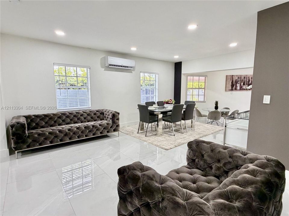 Large-format tile flooring, recessed ceiling lighting, wall-mounted ductless air conditioning unit, and multiple windows with white blinds