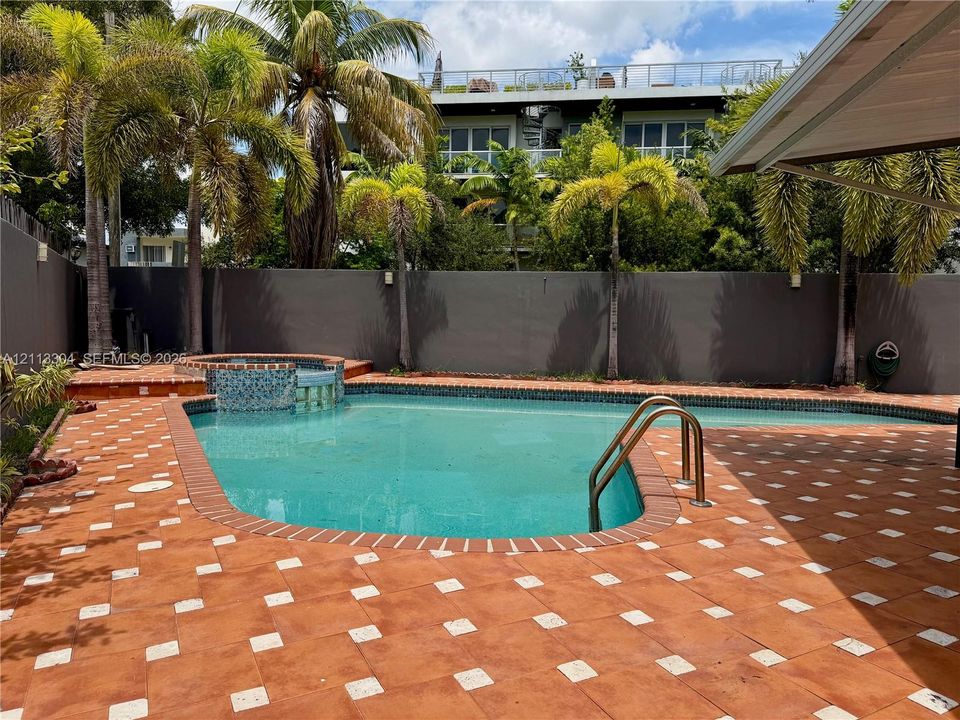 In-ground swimming pool with an integrated spa, mosaic tile detailing, and patterned paver surround