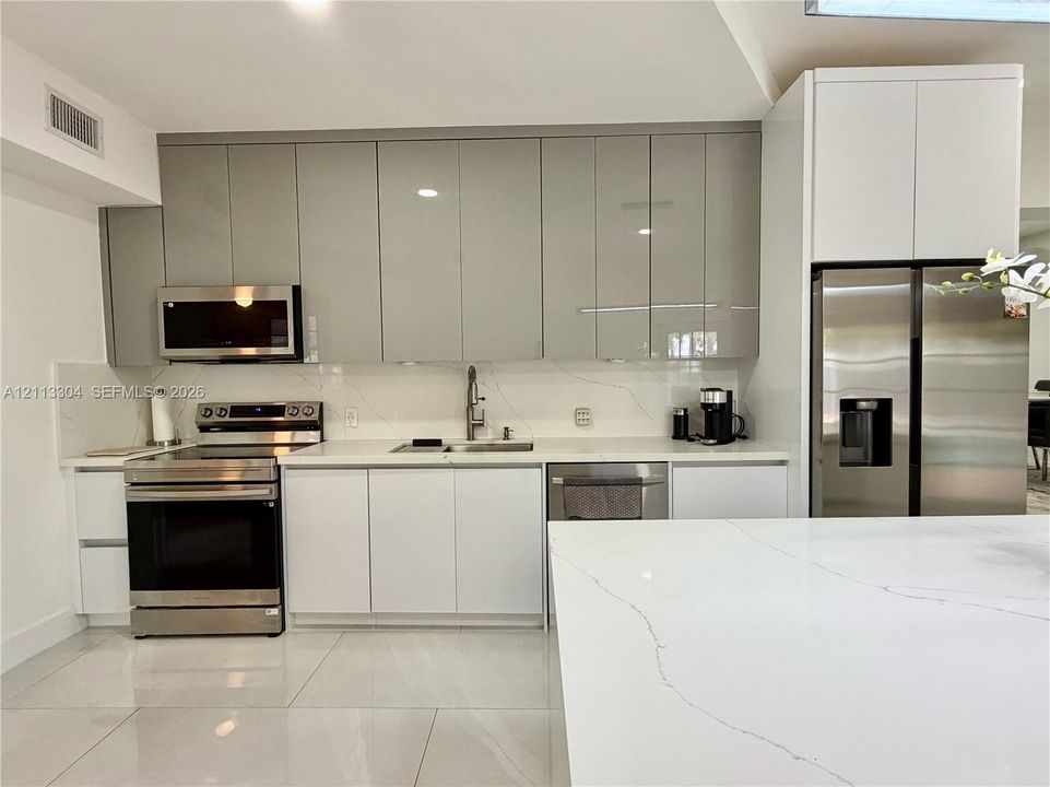 Kitchen featuring high-gloss cabinetry, stone-finish countertops with matching backsplash, stainless steel appliances, and large-format tile flooring