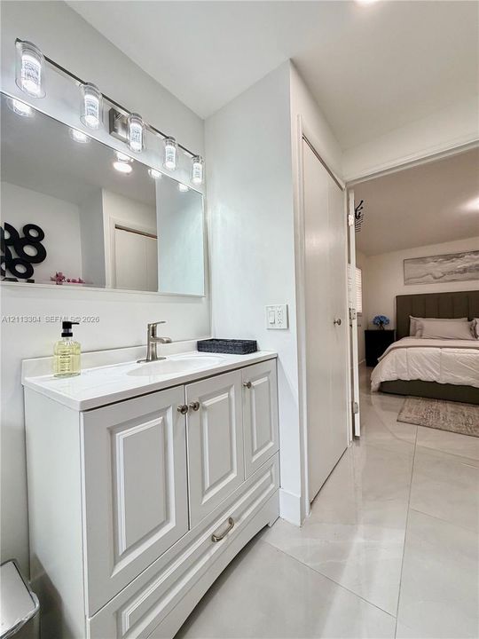 White vanity with shaker-style cabinetry, solid-surface countertop with an integrated sink, polished metal hardware, and a multi-bulb light fixture mounted above a rectangular mirror