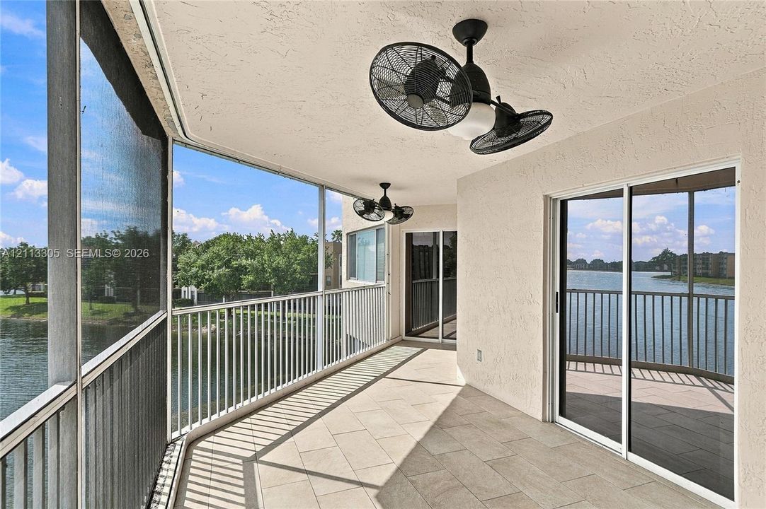 Screened balcony featuring tile flooring, metal railings, dual ceiling-mounted fans, and sliding glass doors