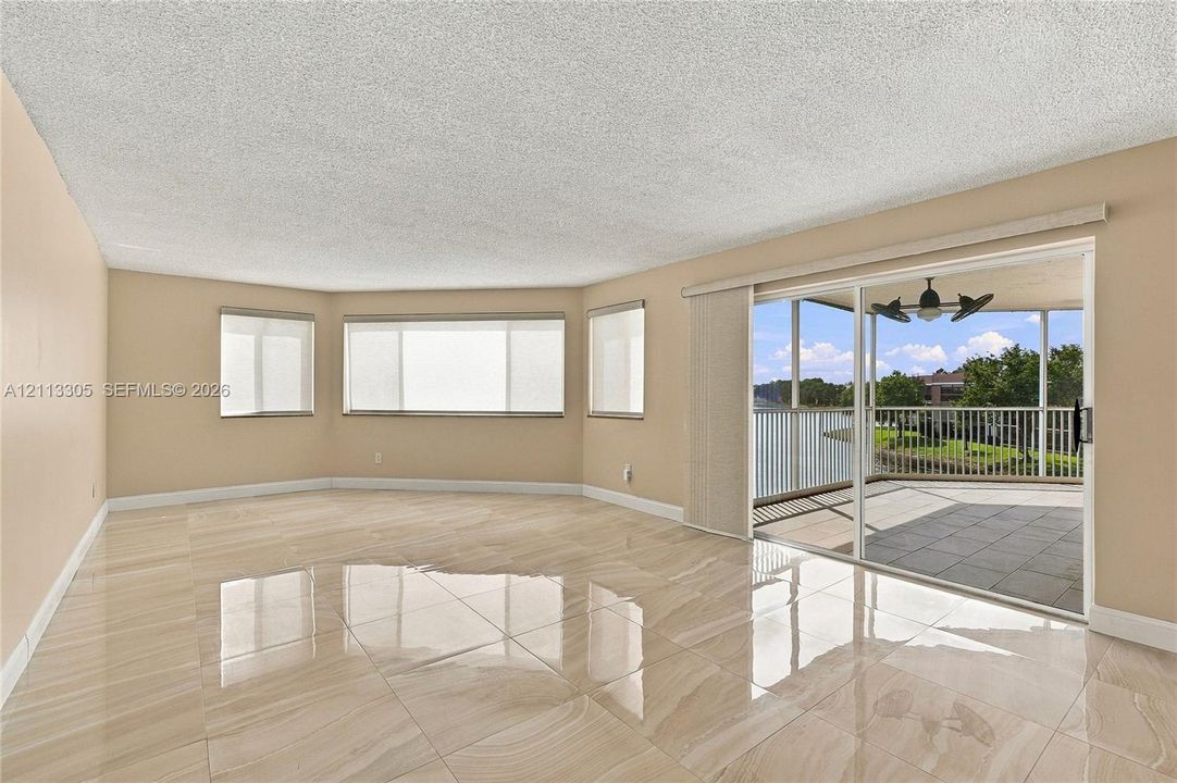 Living area featuring large-format tile flooring, expansive multi-pane windows, and a sliding glass door providing access to a screened-in balcony with ceiling fan