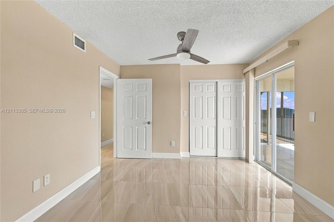Neutral-toned room featuring light-reflective tile flooring, a ceiling fan with integrated lighting, dual-panel closet doors, and sliding glass doors