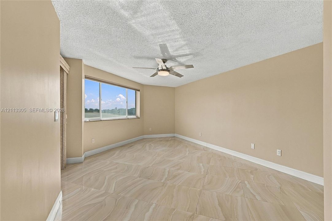 Room featuring large-format tile flooring, a textured ceiling, a ceiling fan with integrated lighting, and a wide window