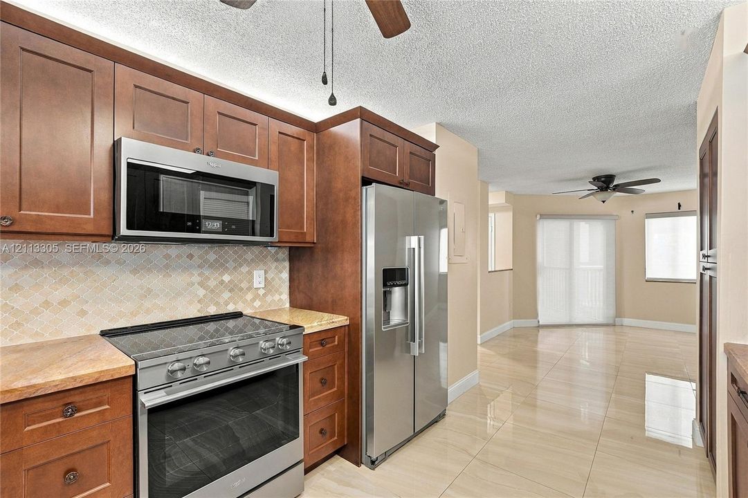 Kitchen featuring medium-tone wood cabinetry, stone countertops, stainless steel appliances, a diamond-pattern tile backsplash, and polished tile flooring