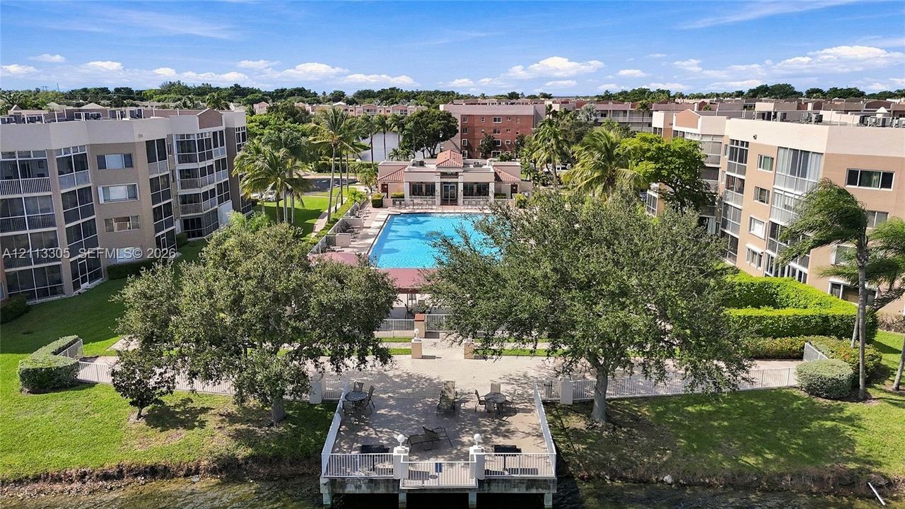 Multi-story residential complex featuring a central outdoor swimming pool, paved sundeck, mature landscaping, and a waterfront pier with built-in grills