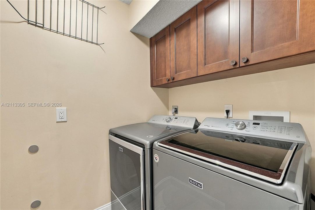 Laundry area featuring warm-toned wood cabinetry, metal wall-mounted storage rack, and stainless steel top-load laundry appliances