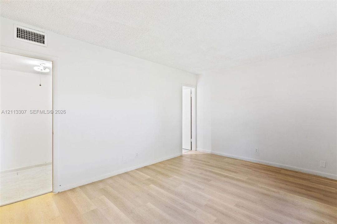 Neutral-toned living space featuring light wood-finish flooring and smooth, monochromatic walls