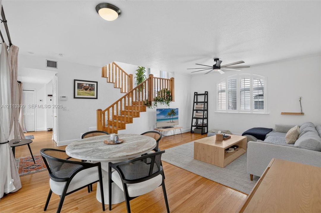 Open floor plan featuring wood-finish flooring, a central staircase with wood railings, and a multi-pane arched window with plantation shutters
