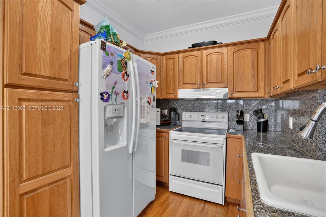 Kitchen featuring wood cabinetry, stone-finish countertops, crown molding, white appliance suite, and a white drop-in sink with a pull-down faucet