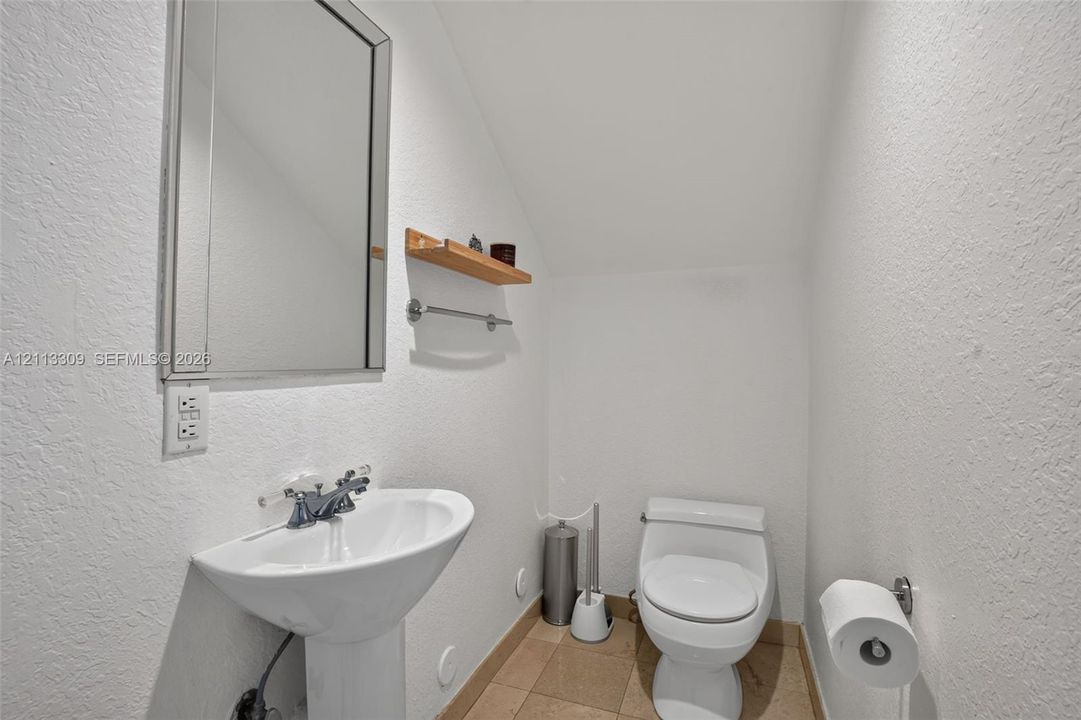 Pedestal sink with dual-handle chrome faucet, wall-mounted rectangular mirror, wood-finish wall shelving, and tile flooring