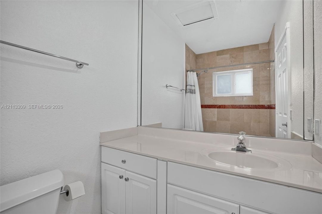 Bathroom featuring a white vanity with a solid surface countertop, an integrated sink, a full-width vanity mirror, and a tub-shower combination with tile surround