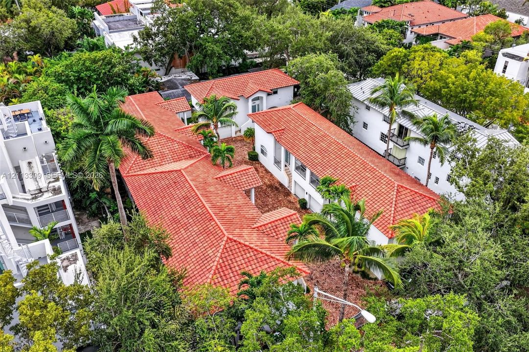 Aerial perspective of a multi-structure property featuring red clay tile roofing, white stucco exteriors, and established mature landscaping