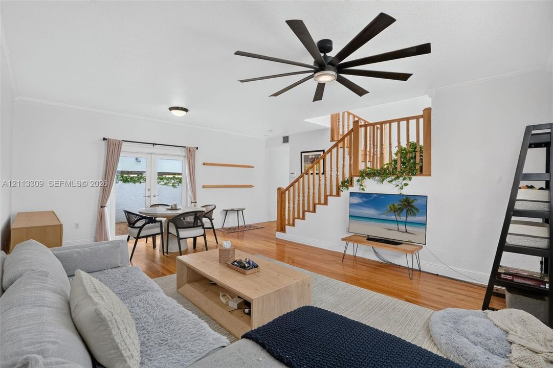 Wood-finish flooring, multi-blade matte black ceiling fan, and wooden staircase featuring a matching railing